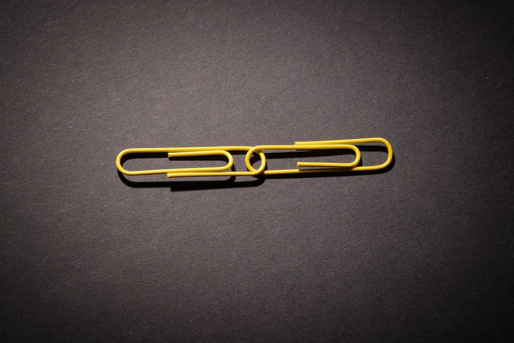 Two Yellow Paper Clips Linked On Dark Background